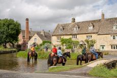 IMM 2019 Bristol -  Classic Car Road Trip: Horses in the river Eye, the Old Mill in Lower Slaughter in the background. In the 14th century, the mill became...